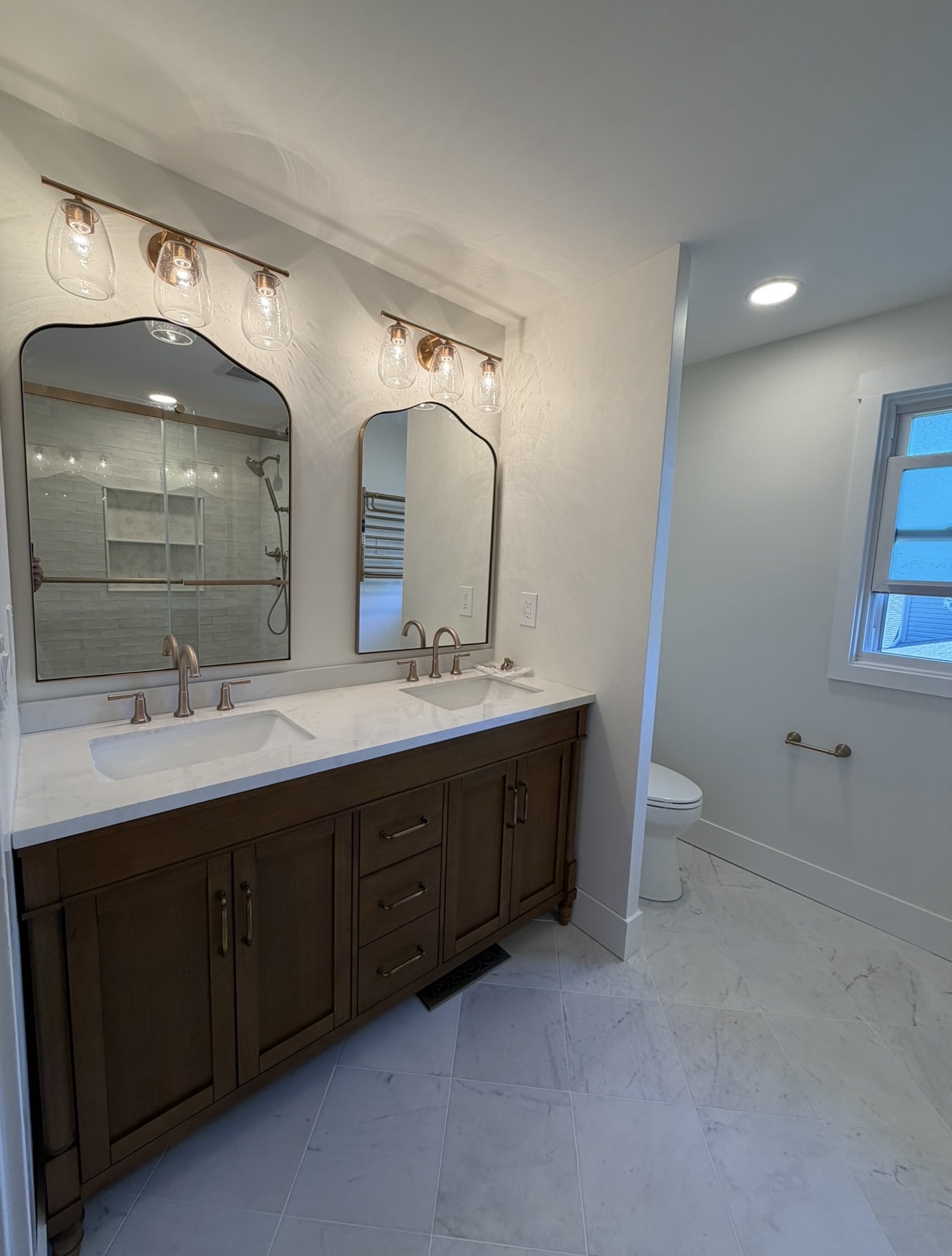 Double-vanity bathroom with arched mirrors, marble tile floor and dark wood cabinetry