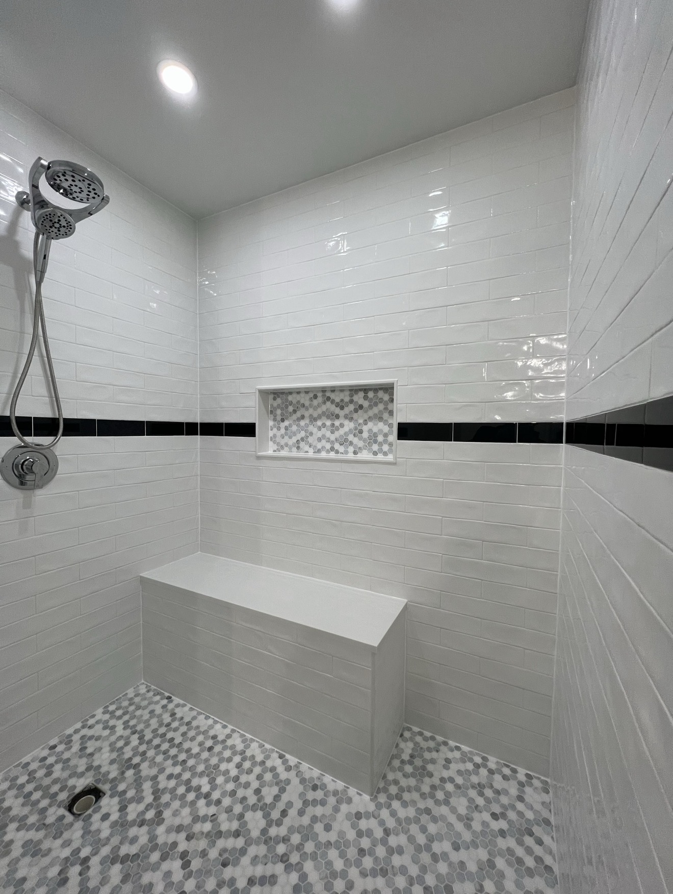 Walk-in tile shower with white subway tile, black accent stripe and hex mosaic floor