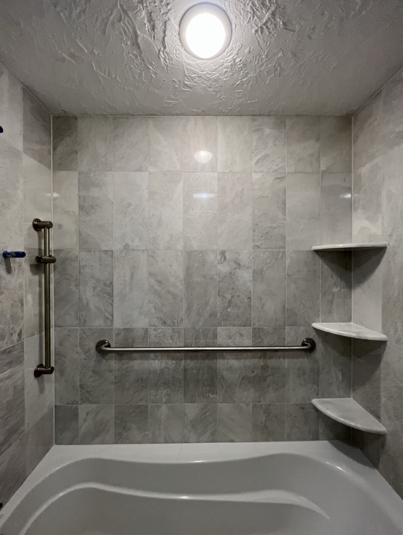 Tub-shower combo with large-format gray marble tile surround and corner shelving