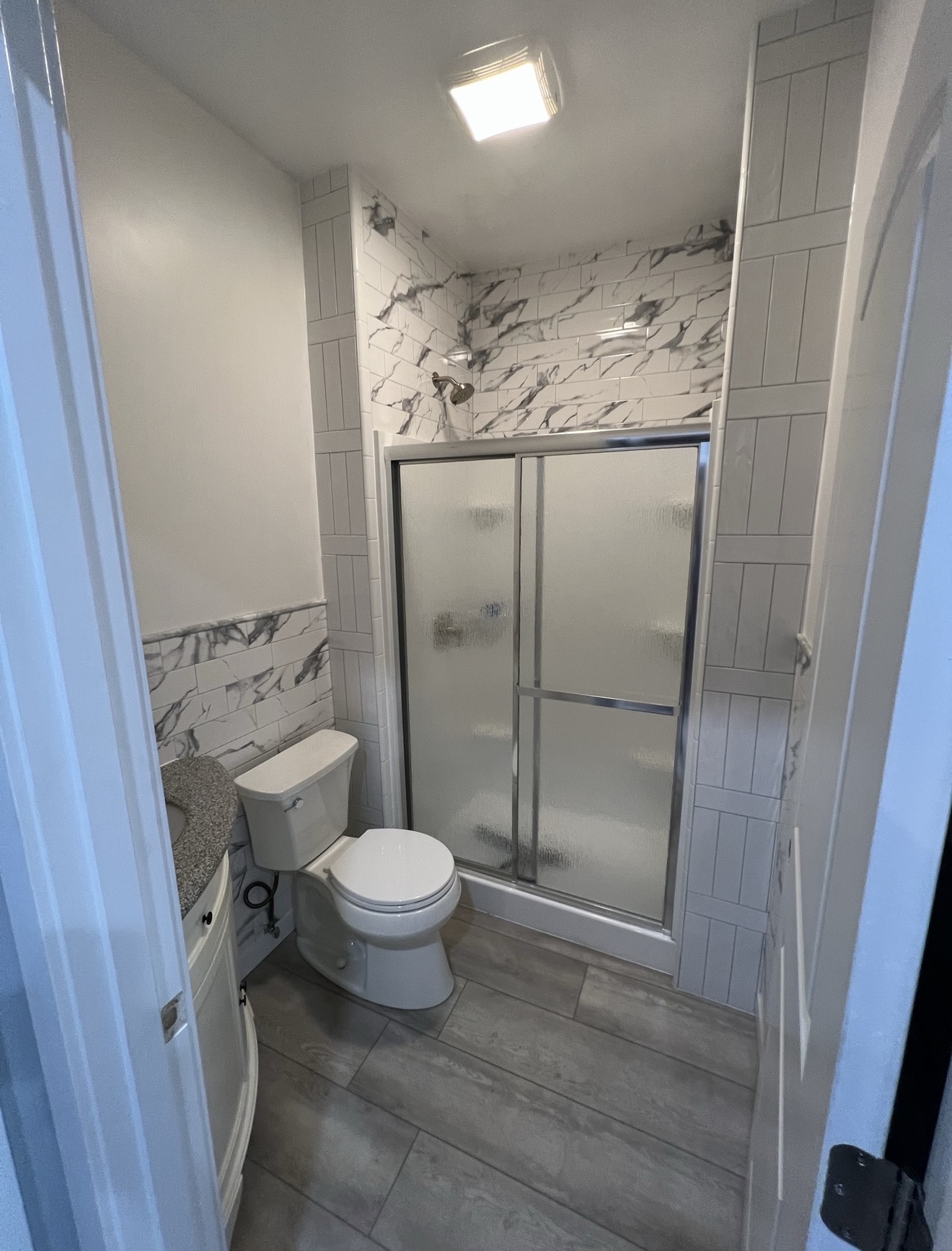 Bathroom with marble subway tile shower, sliding glass doors and gray plank floor