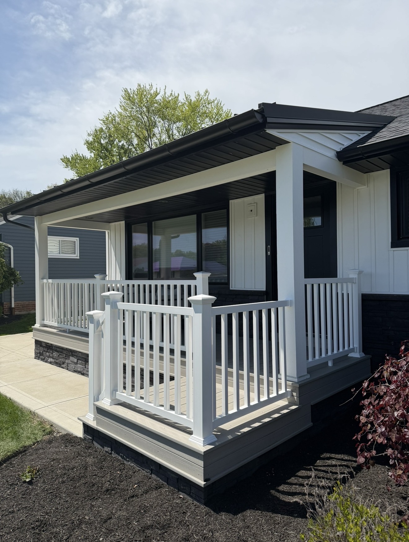 Covered front porch with white railings, black trim and board-and-batten siding