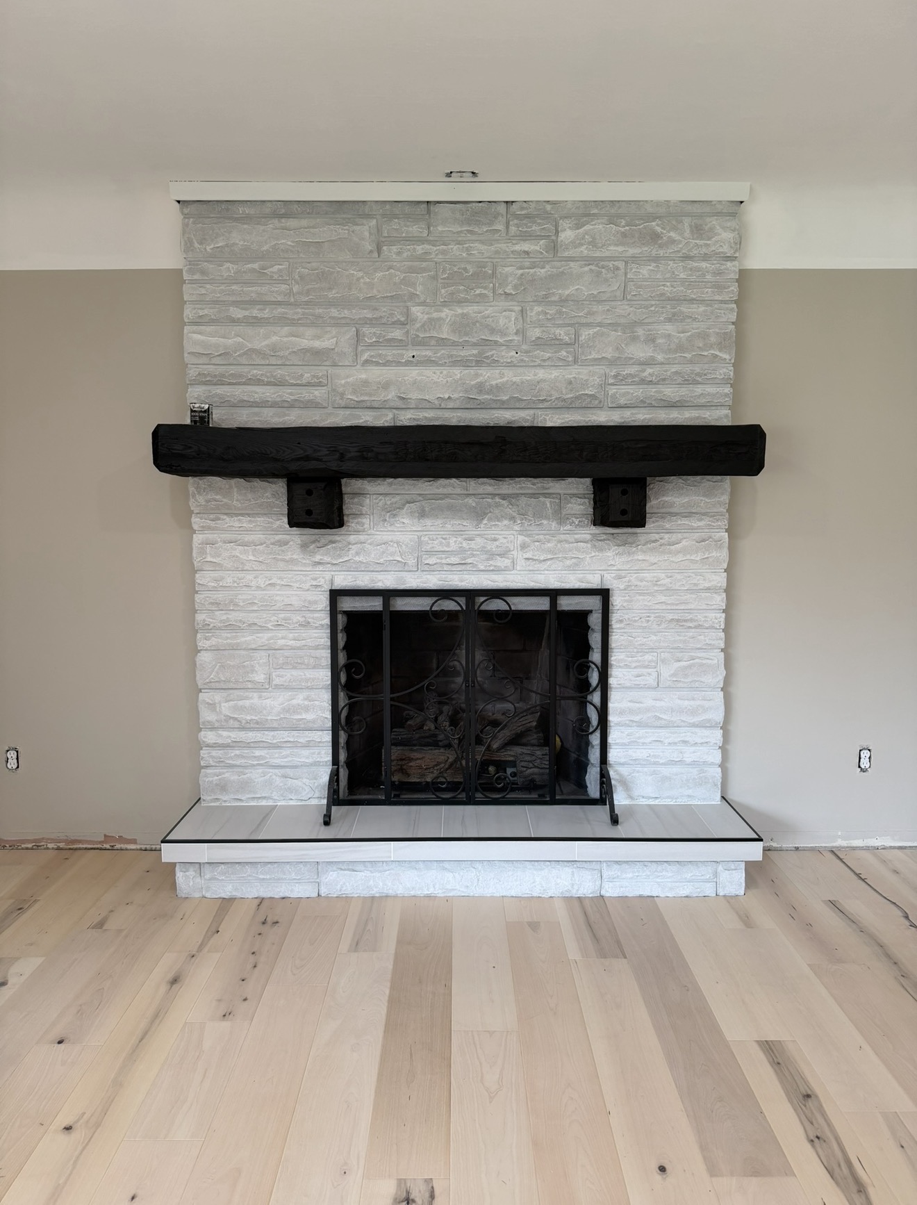 Stone fireplace with charred wood mantel and wide-plank hardwood flooring