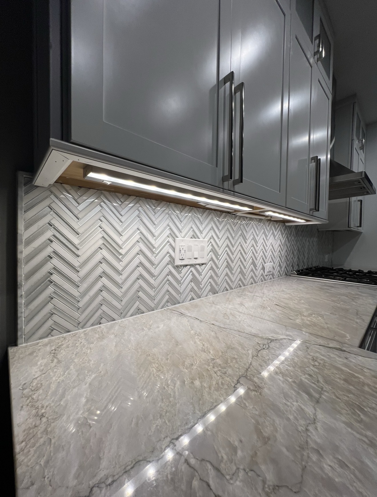 Kitchen close-up with gray shaker cabinets, herringbone mosaic backsplash and quartzite counters